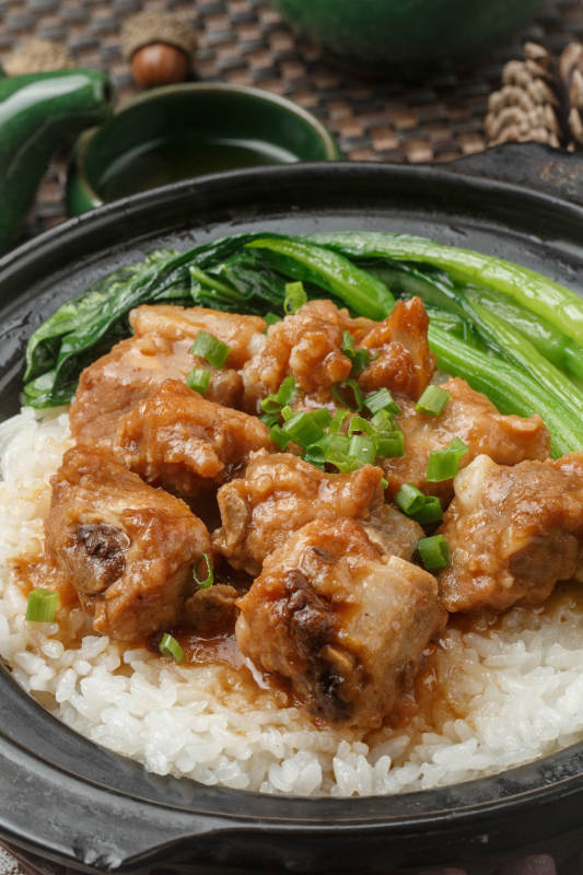 黑色砂锅装的排骨芥蓝煲仔饭摆放在餐布上图片