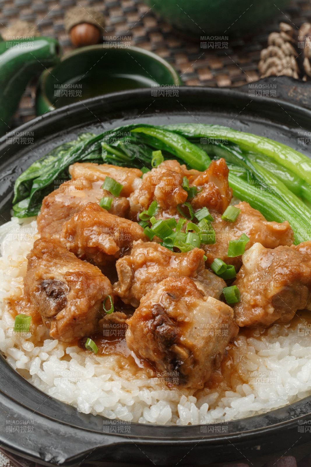 黑色砂锅装的排骨芥蓝煲仔饭摆放在餐布上图片