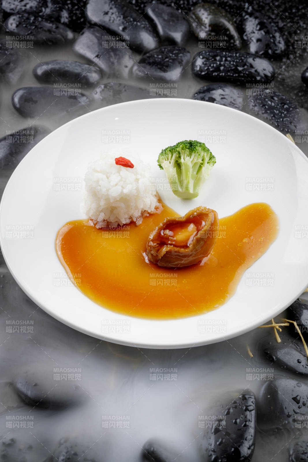 鲍汁捞饭摆放在干冰缭绕的黑色鹅卵石上图片