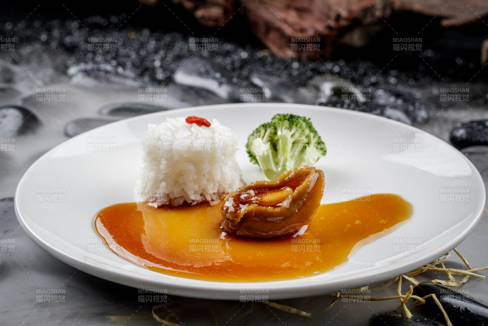 鲍汁捞饭摆放在干冰缭绕的黑色鹅卵石上图片