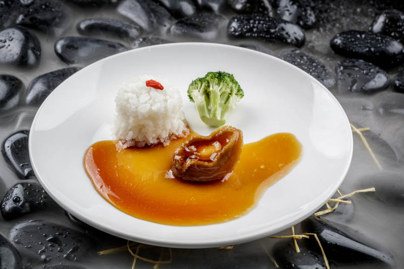 鲍汁捞饭摆放在干冰缭绕的黑色鹅卵石上图片