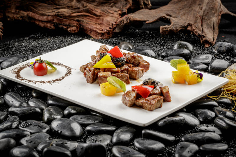 黑蒜牛小排摆放在黑色鹅卵石上图片