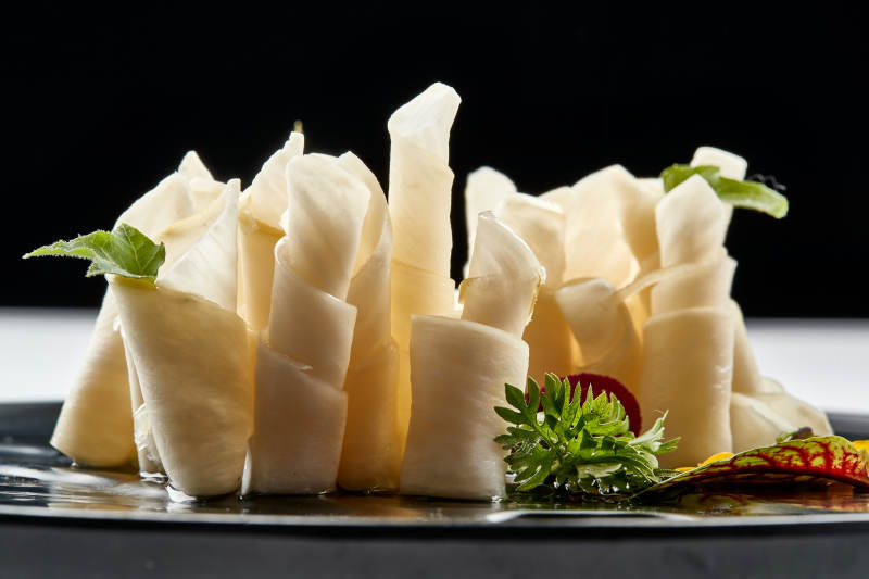 黑色瓷餐具装的鲜杏鲍菇刺身卷图片