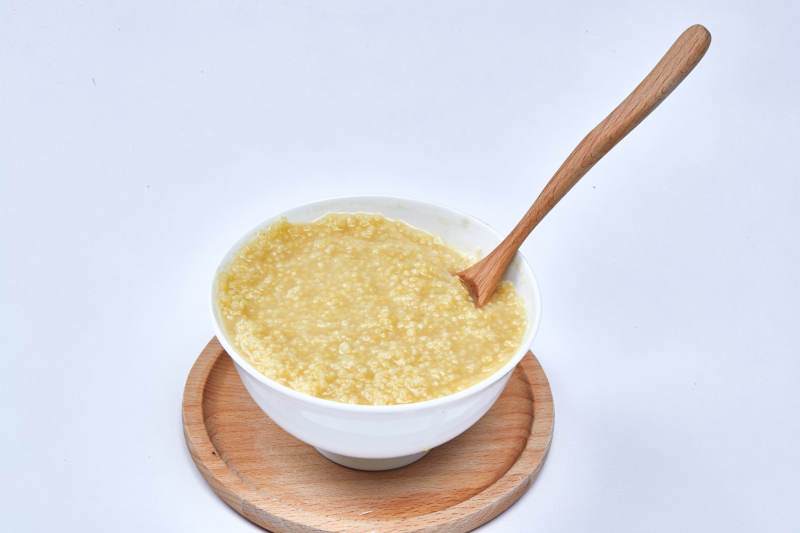 手持木勺㧟起的美味香浓小米粥图片