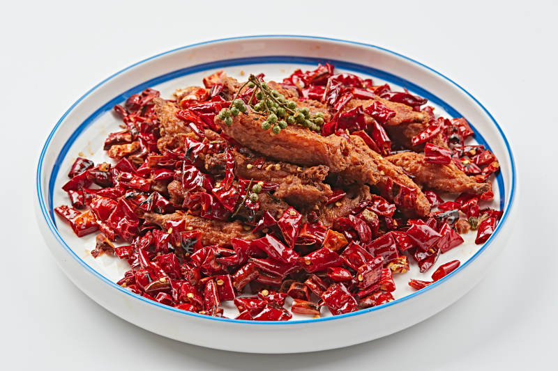 白色瓷盘装的川香油炸麻辣鸡翅中图片