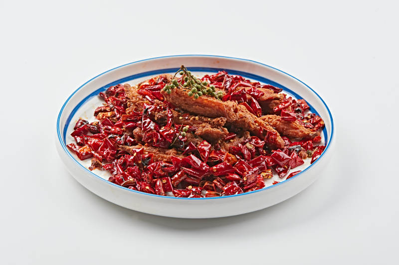 白色瓷盘装的川香油炸麻辣鸡翅中图片