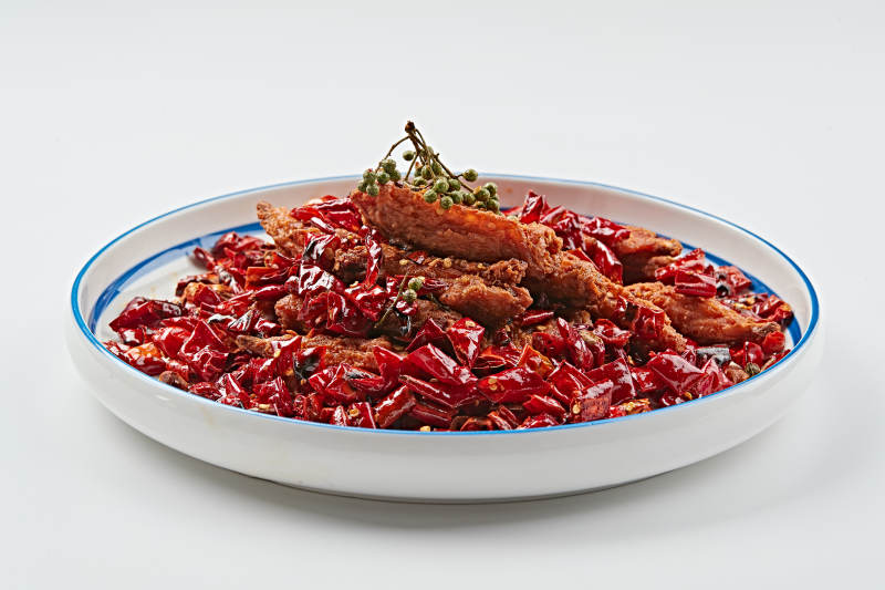 白色瓷盘装的川香油炸麻辣鸡翅中图片