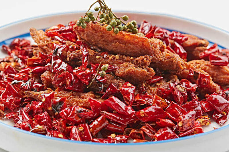 白色瓷盘装的川香油炸麻辣鸡翅中图片