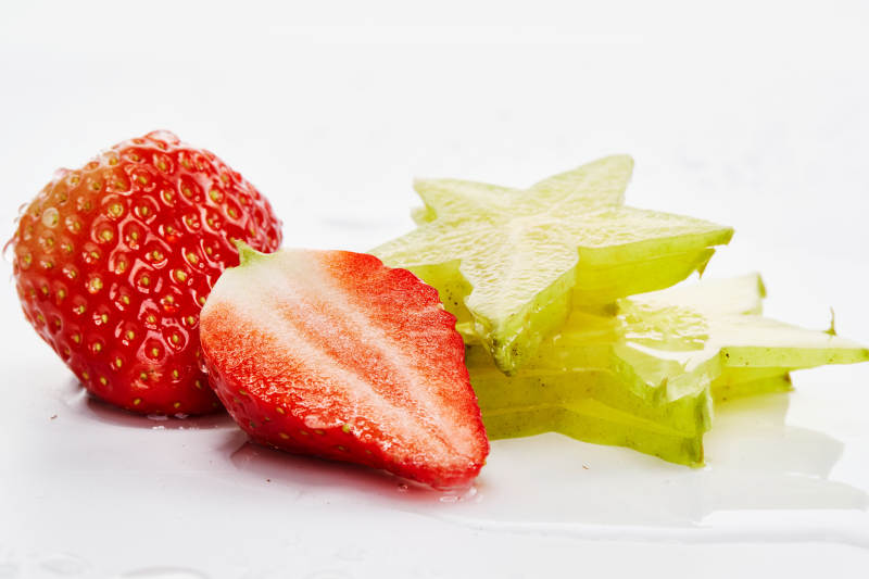 白色背景上摆放的新鲜洋桃和草莓及切片图片