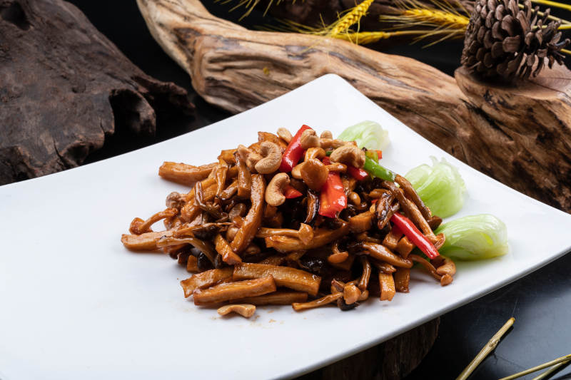 长方形瓷盘装的腰果杭椒杏鲍菇摆放在黑色背景上图片