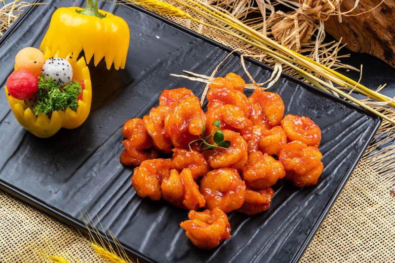 黑色石盘装的宫爆大虾球摆放在麻布垫子上图片