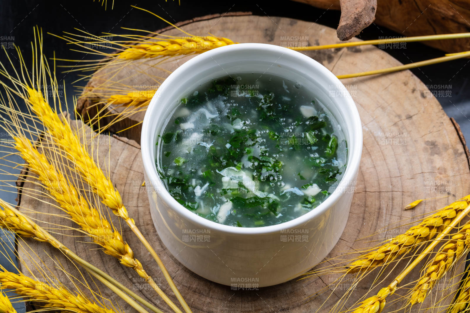 汤盅装的菠菜蛋花羹摆放在樟木砧板上图片