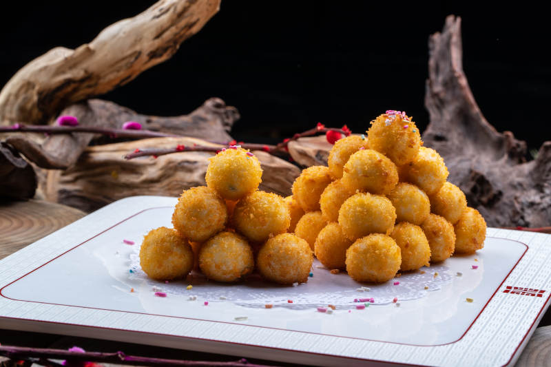 方形瓷盘装的黄金炸汤圆摆放在樟木砧板上图片