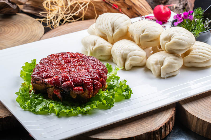 长方形瓷盘装的花馍夹酱肉摆放在樟木砧板上图片