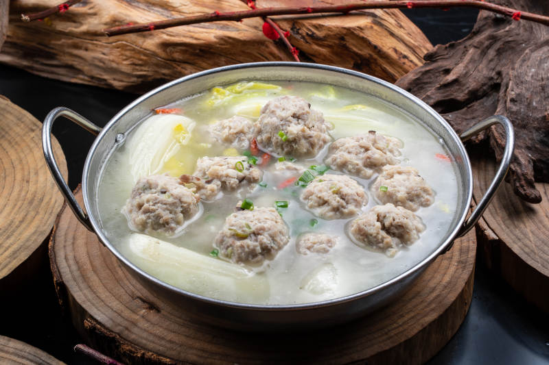 铁锅装的锅仔白菜汤汆丸子摆放在樟木砧板上图片