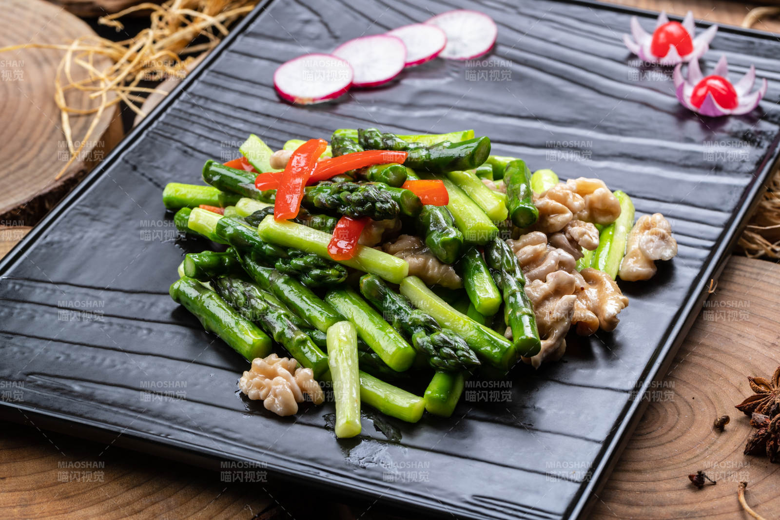 黑色石盘装的鲜芦笋桃仁摆放在樟木砧板上图片