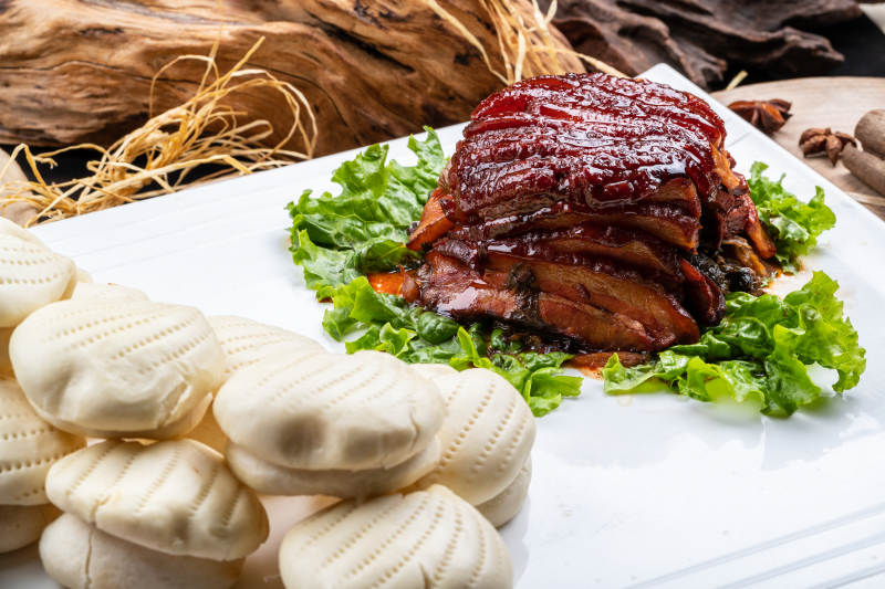 长方形瓷盘装的花馍夹酱肉摆放在樟木砧板上图片