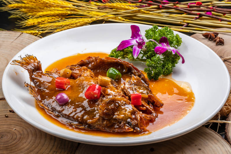 白色圆盘装的红烧罗非鱼摆放在樟木砧板上图片