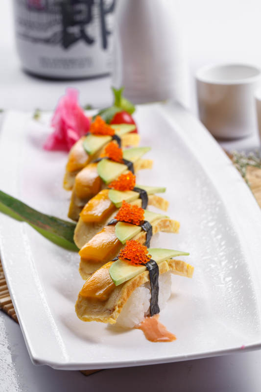 烧蛋蟹子芒果手握寿司摆放在寿司帘上图片