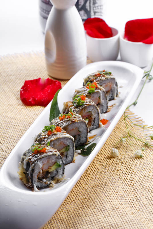 椭圆长瓷盘装的鹅肝手卷寿司摆放在草垫上图片