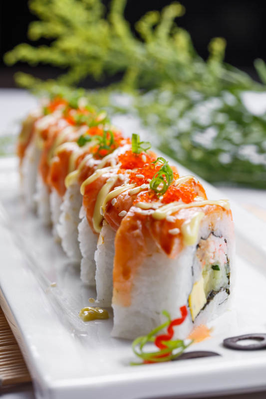 长方形瓷盘装的灸三文鱼卷摆放在寿司帘上图片