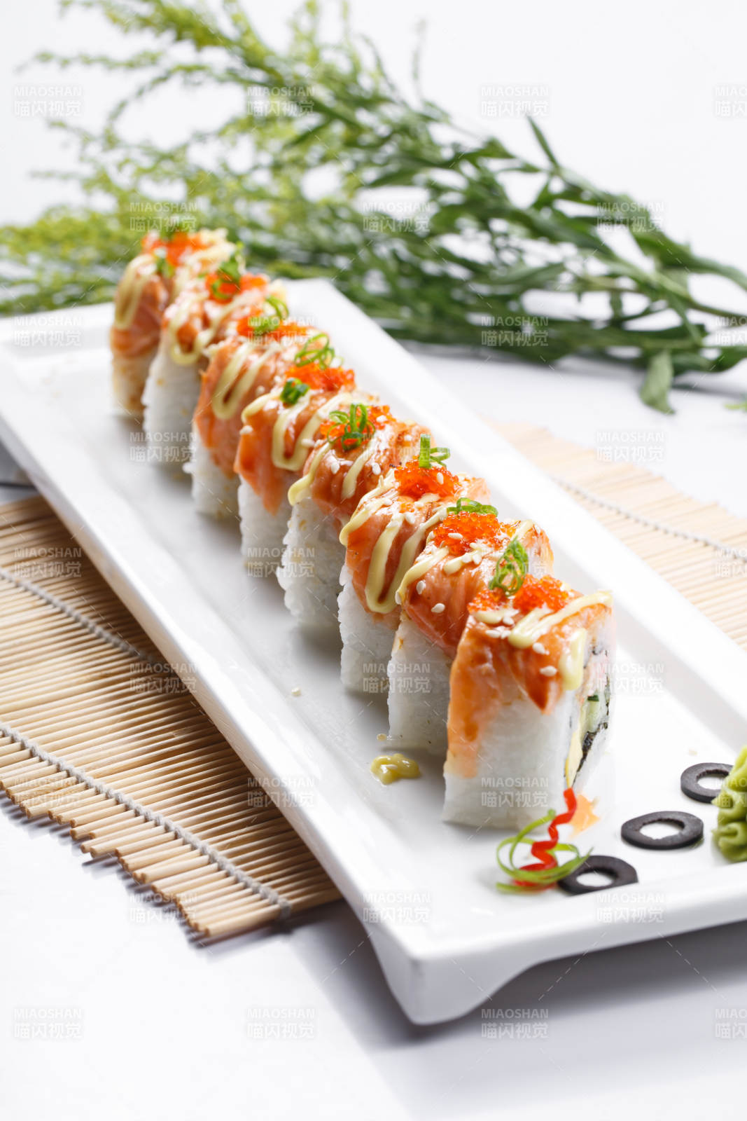 长方形瓷盘装的灸三文鱼卷摆放在寿司帘上图片