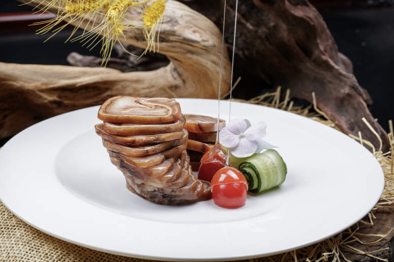 白色圆盘装的烟熏猪耳卷摆放在麻布垫子上图片