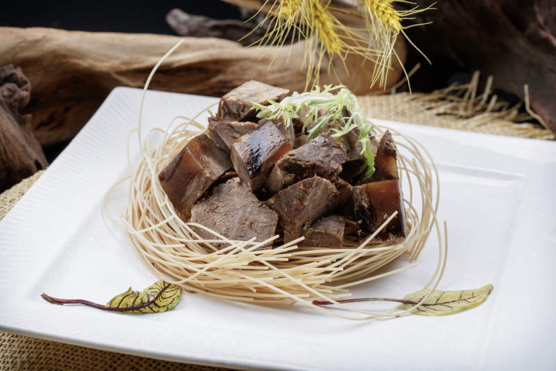 方形瓷盘装的老卤汤牛方粒摆放在麻布垫子上图片