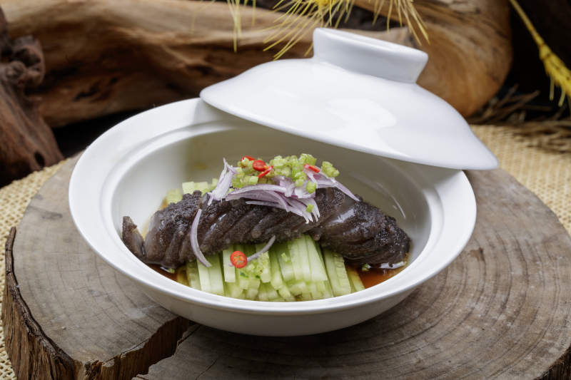 白色汤碗装的锅烧大海参摆放在樟木砧板上图片