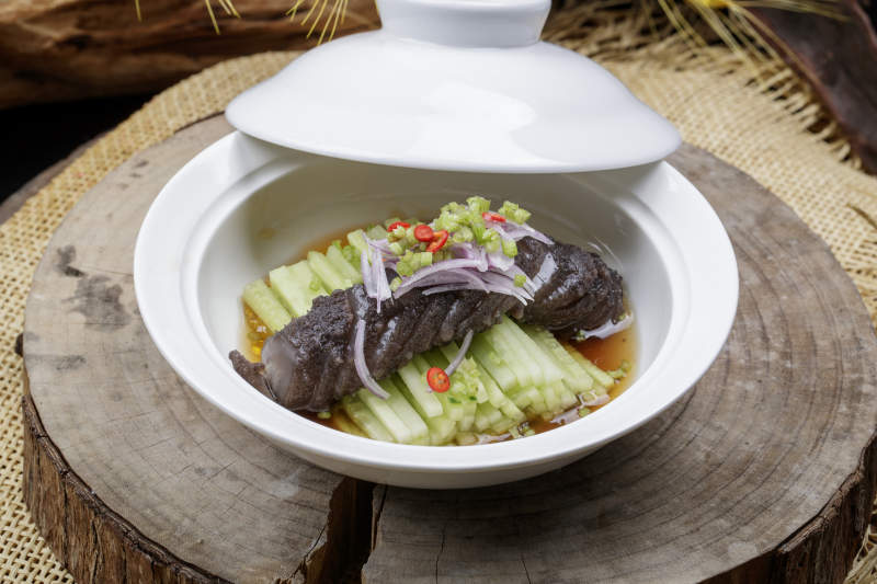 白色汤碗装的锅烧大海参摆放在樟木砧板上图片