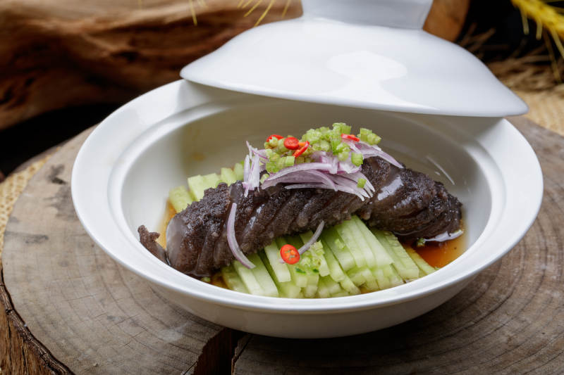 白色汤碗装的锅烧大海参摆放在樟木砧板上图片