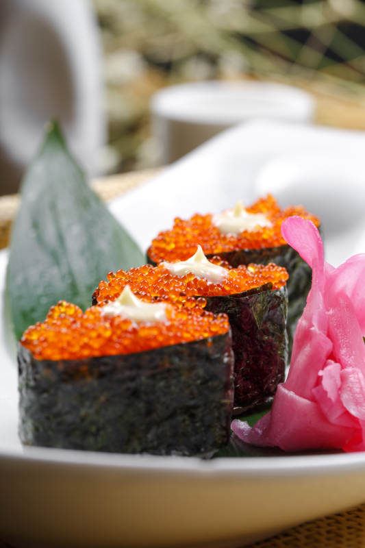 鹅颈瓷盘装的蟹子军舰手握寿司摆放在石头上图片