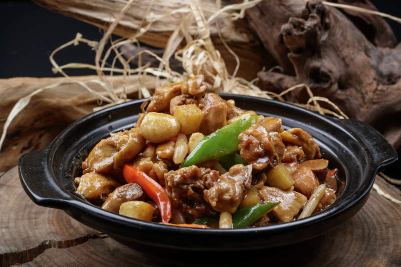 黑色砂锅装的砂锅蒜香鸡摆放在樟木砧板上图片