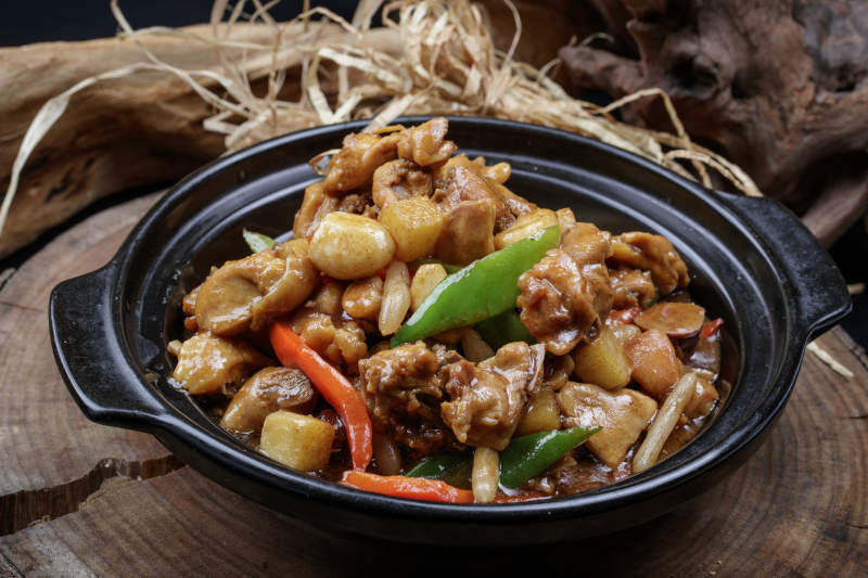 黑色砂锅装的砂锅蒜香鸡摆放在樟木砧板上图片