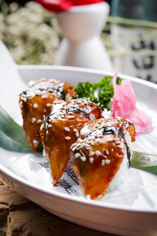 鹅颈白瓷盘装的烤鳗鱼手握寿司摆放在石头上图片