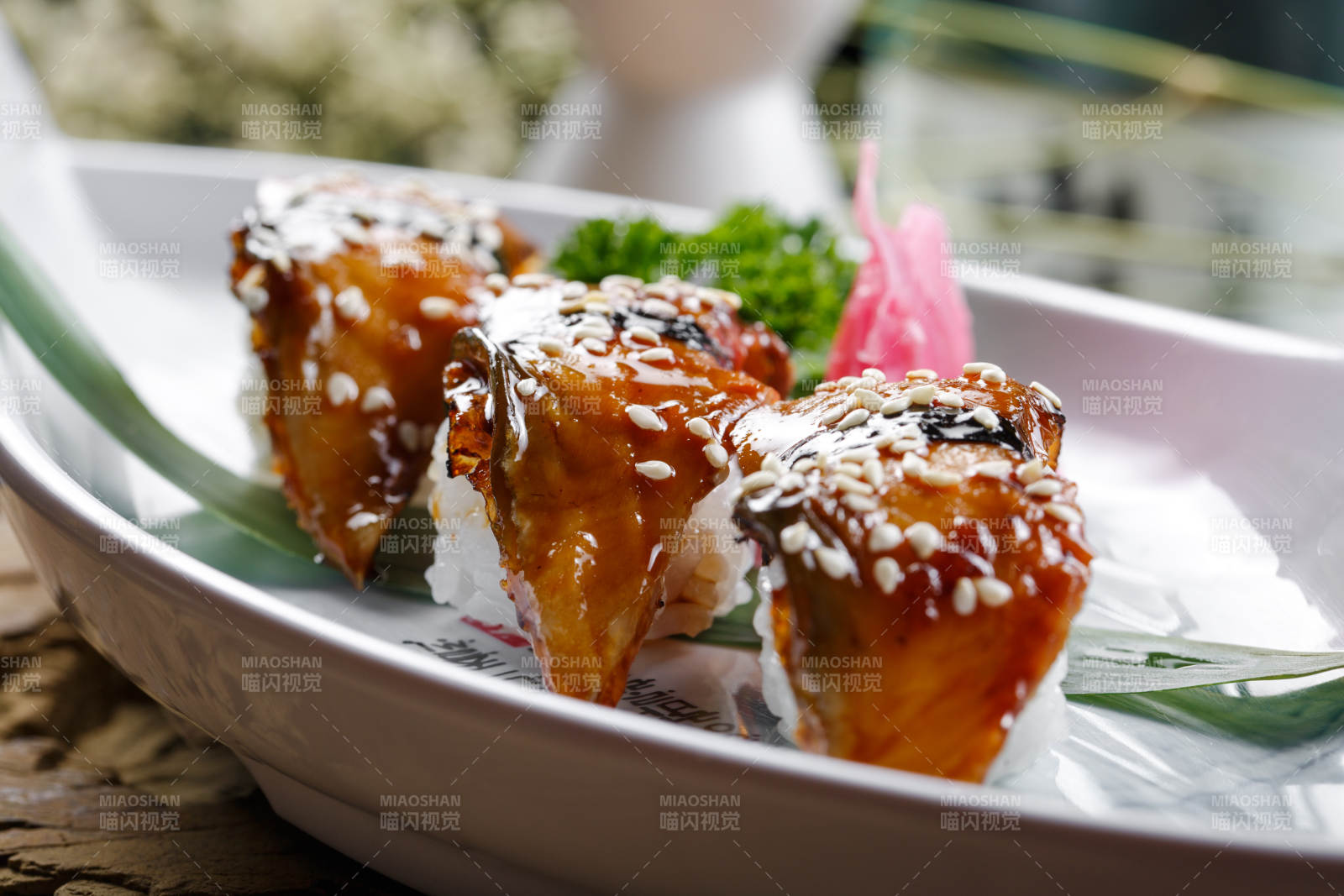 鹅颈白瓷盘装的烤鳗鱼手握寿司摆放在石头上图片