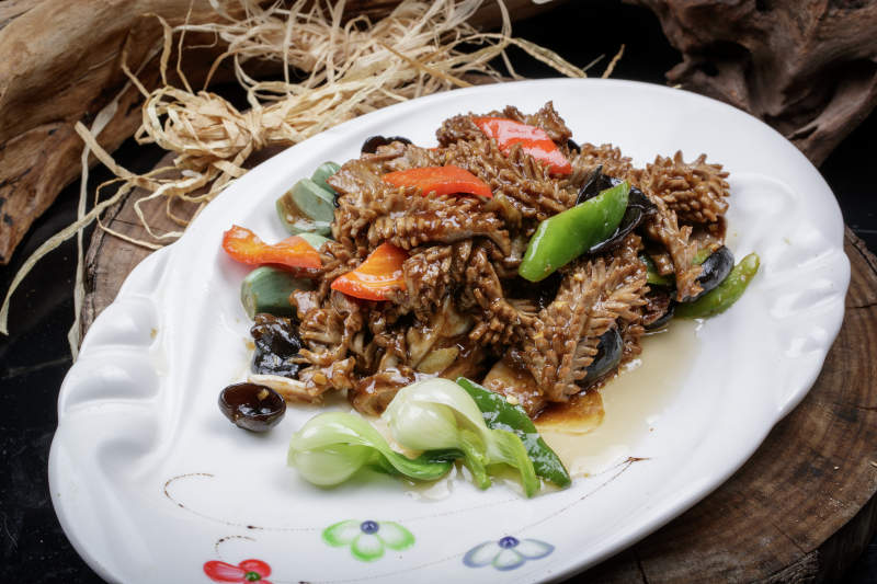 椭圆瓷盘装的腊八蒜炒腰花摆放在樟木砧板上图片