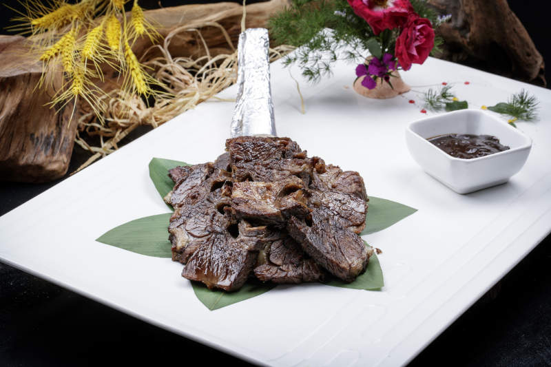 方形瓷盘装的炭烤牛肋排摆放在黑色背景上图片