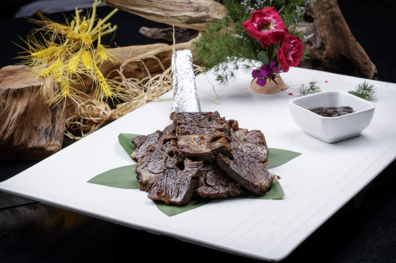 方形瓷盘装的炭烤牛肋排摆放在黑色背景上图片