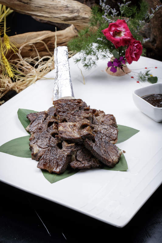 方形瓷盘装的炭烤牛肋排摆放在黑色背景上图片