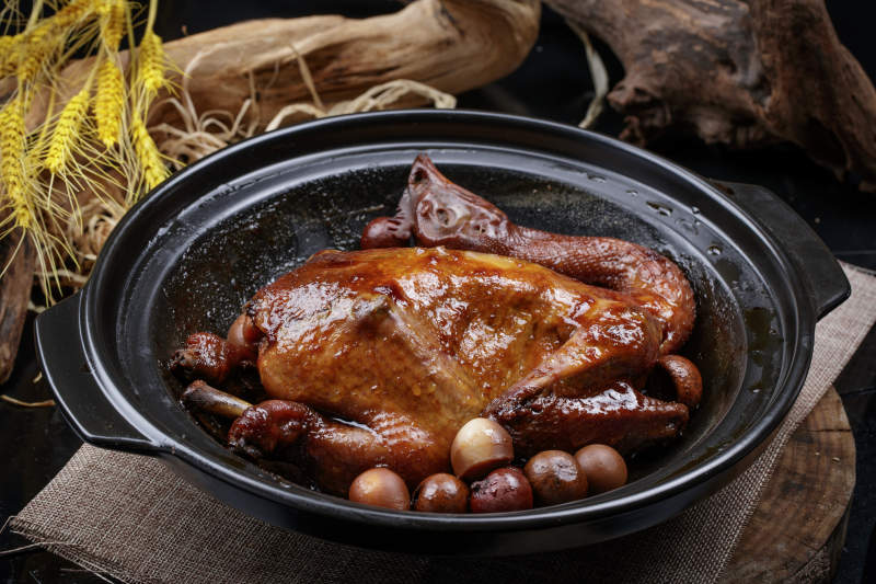 黑色砂锅装的生噘鸡煲摆放在幕布垫子上图片