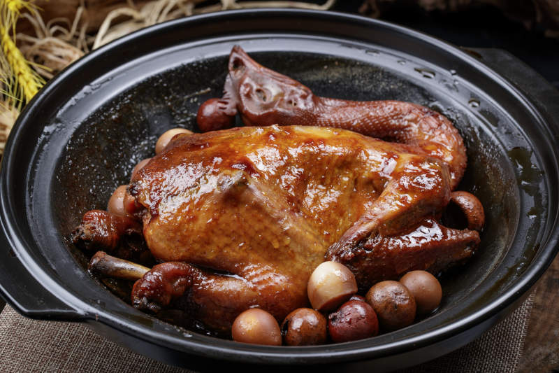 黑色砂锅装的生噘鸡煲摆放在幕布垫子上图片