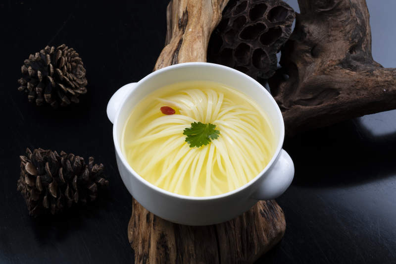 白色汤盅装的文菊豆腐养生汤摆放在崖柏根上图片