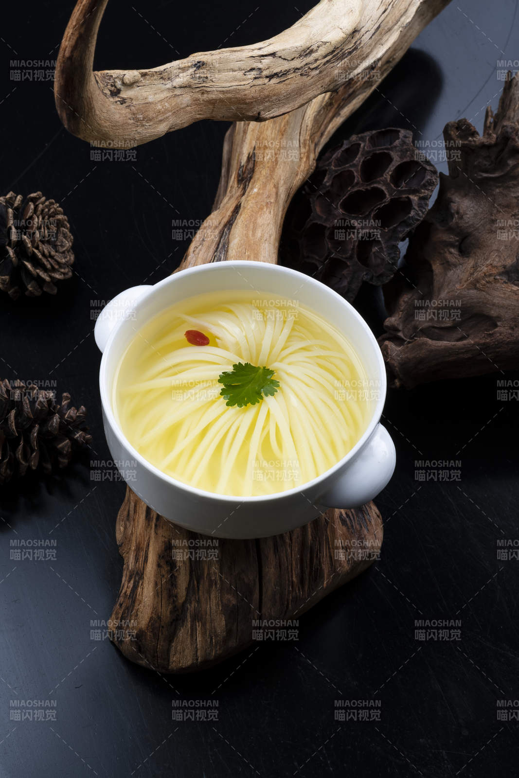 白色汤盅装的文菊豆腐养生汤摆放在崖柏根上图片