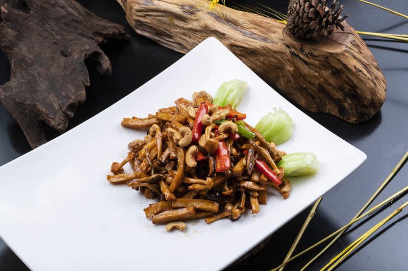 长方形瓷盘装的腰果杭椒杏鲍菇摆放在黑色背景上图片