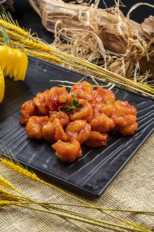 黑色石盘装的宫爆大虾球摆放在麻布垫子上图片