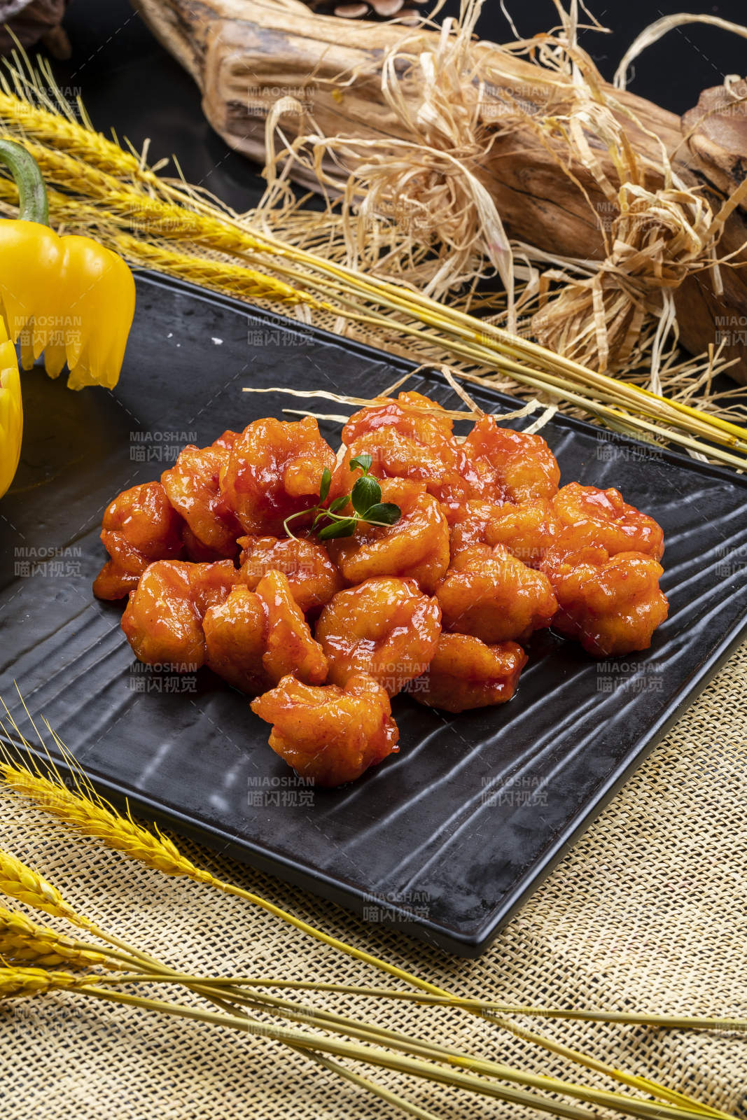 黑色石盘装的宫爆大虾球摆放在麻布垫子上图片