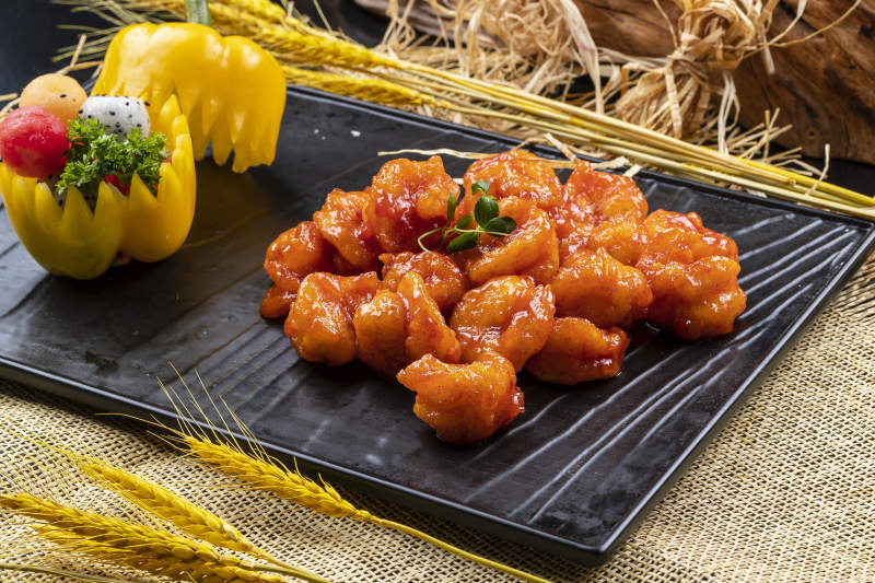 黑色石盘装的宫爆大虾球摆放在麻布垫子上图片