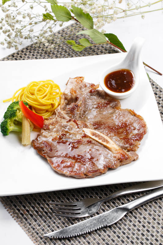 方形瓷盘装的新西兰T骨牛排摆放在餐垫上图片