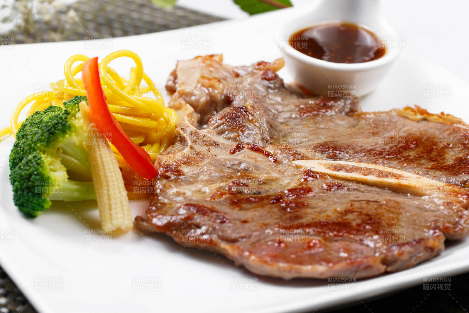 方形瓷盘装的新西兰T骨牛排摆放在餐垫上图片